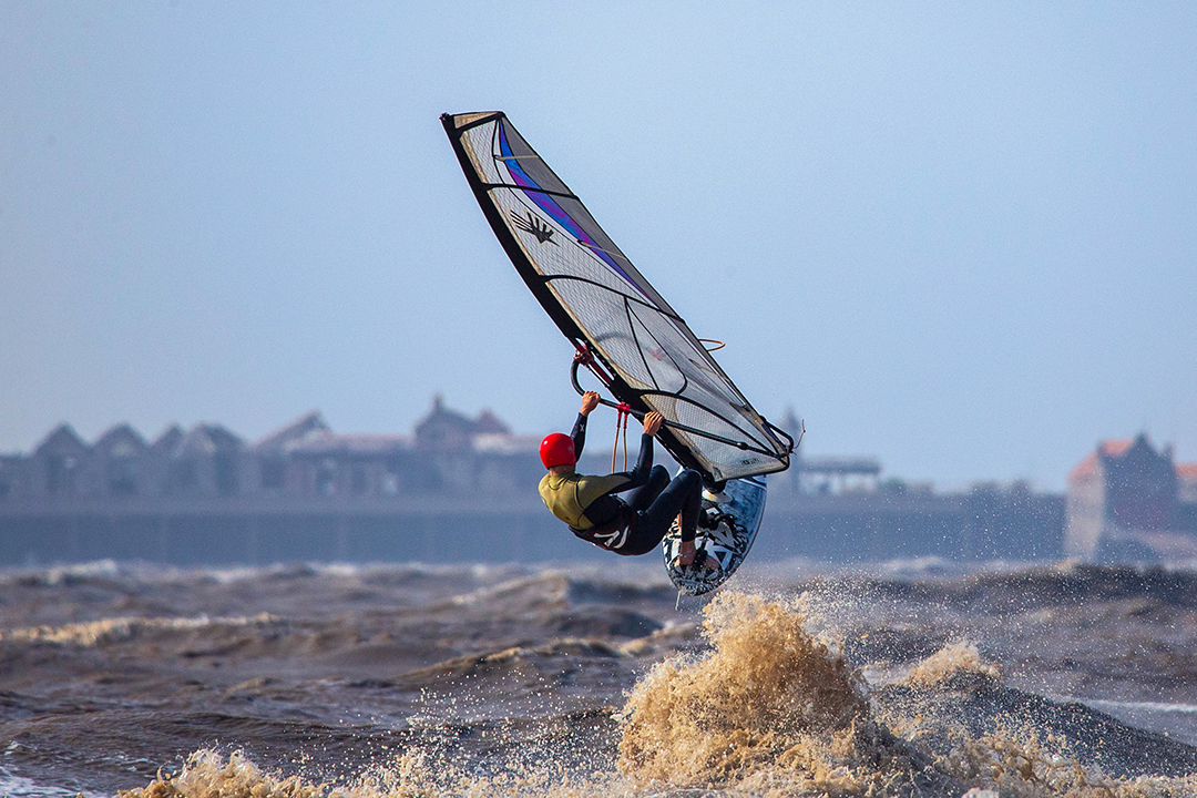 A windsurfer holds onto his sail as he is lifted out of the water